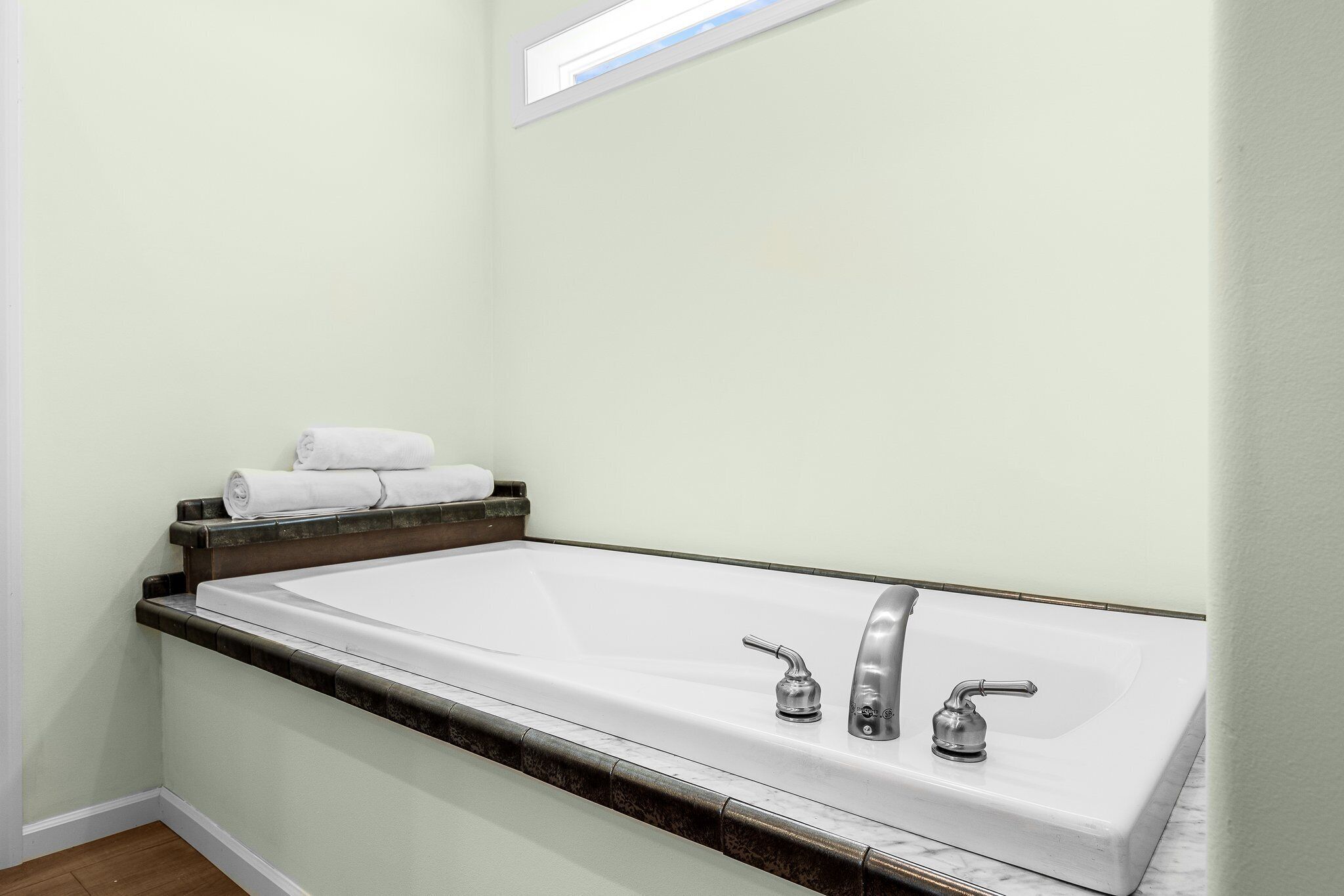 A bathroom with a large bathtub, two faucets, and a towel rack with folded towels.