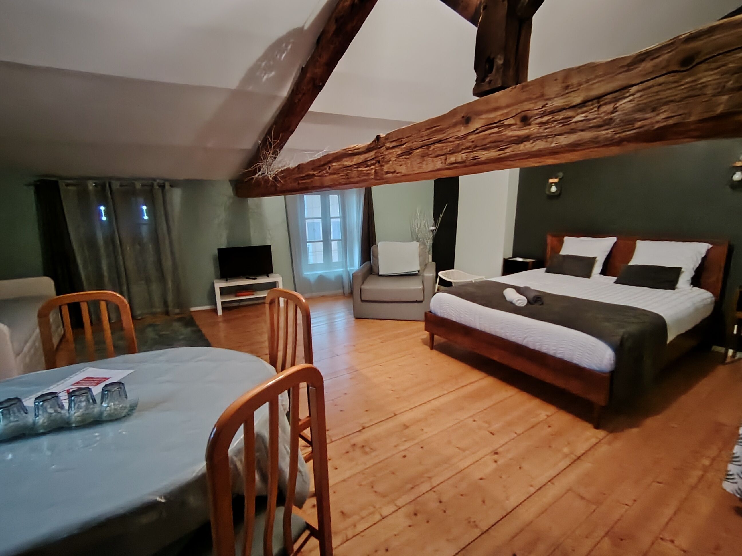 Una habitación acogedora con techo de madera, una cama con almohadas, un televisor sobre un mueble, una silla y una mesa con camino de mesa.