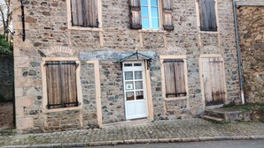Ein Steinhaus mit einer weißen Eingangstür in der Mitte, flankiert von Holzläden, und einer Kopfsteinpflasterstraße davor.