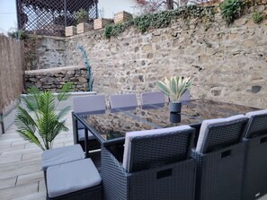 Un patio al aire libre con mobiliario de mimbre y un muro de piedra de fondo.