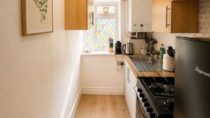 A kitchen with wooden cabinets, a stove, a refrigerator, and a window with a colorful diamond pattern. - Paddington Studios • by Oxford Street & Marylebone (London)