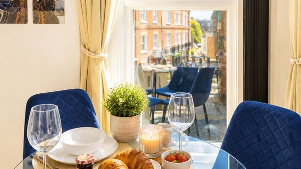 A dining table with plates, glasses, a candle, and pastries in a room with a view of buildings through a window. - Paddington Studios • by Oxford Street & Marylebone (London)