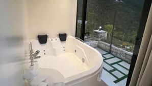 Une salle de bain moderne dotée d’une baignoire sur pieds, d’une douche et d’une grande fenêtre offrant une vue sur un paysage montagneux.