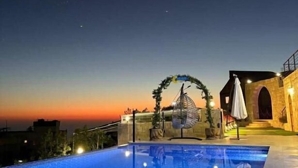 Une piscine nocturne offrant une vue dégagée sur le ciel, une arche décorative et un bâtiment doté d’un balcon.