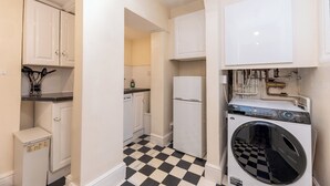 A compact kitchen with white cabinets, a washing machine, and a small refrigerator. - Two Bedroom Flat - Next to West Kensington Station - Pass the Keys (London)
