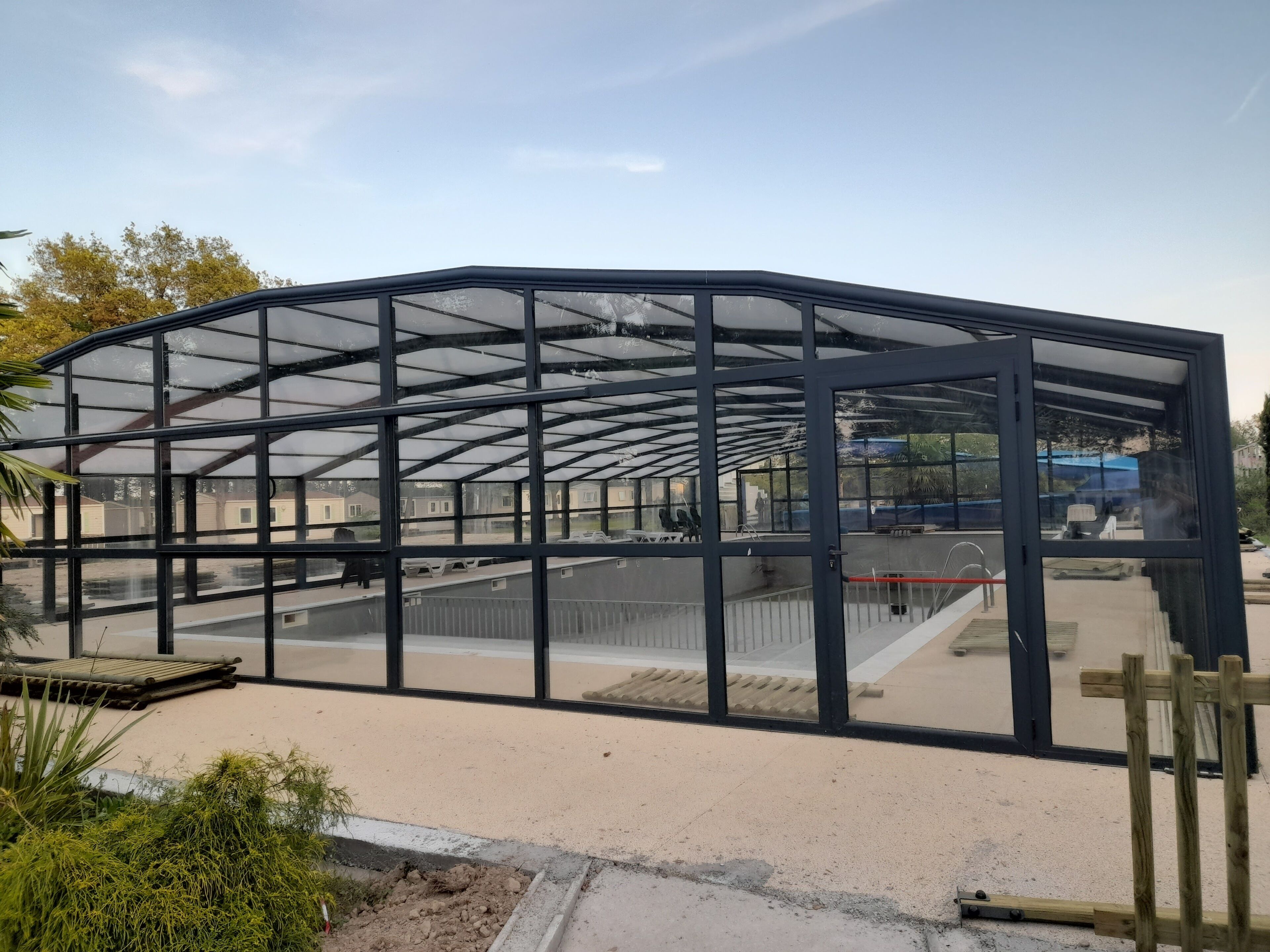 Een grote, open constructie met een metalen frame en glazen panelen, waarschijnlijk een kas of conservatorium.