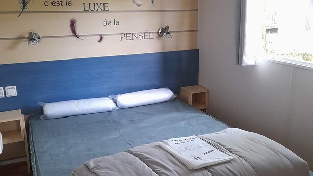 Un dormitorio con una cama, cabecera de madera con plumas decorativas y texto, mesitas de noche y una ventana con cortinas.