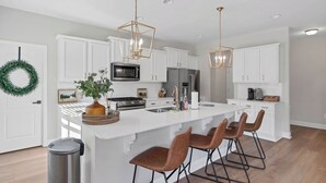 A modern kitchen with white cabinetry, stainless steel appliances, a central island with bar stools, and pendant lighting. - Spacious 6-bedroom house near Pinehurst (Southern Pines)