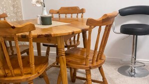 Een eetgedeelte met een houten tafel, stoelen, een vaas met bloemen en een barkruk.