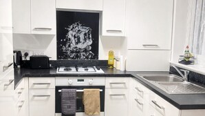 Een moderne keuken met witte kastjes, een zwarte spatwand en een gasfornuis.