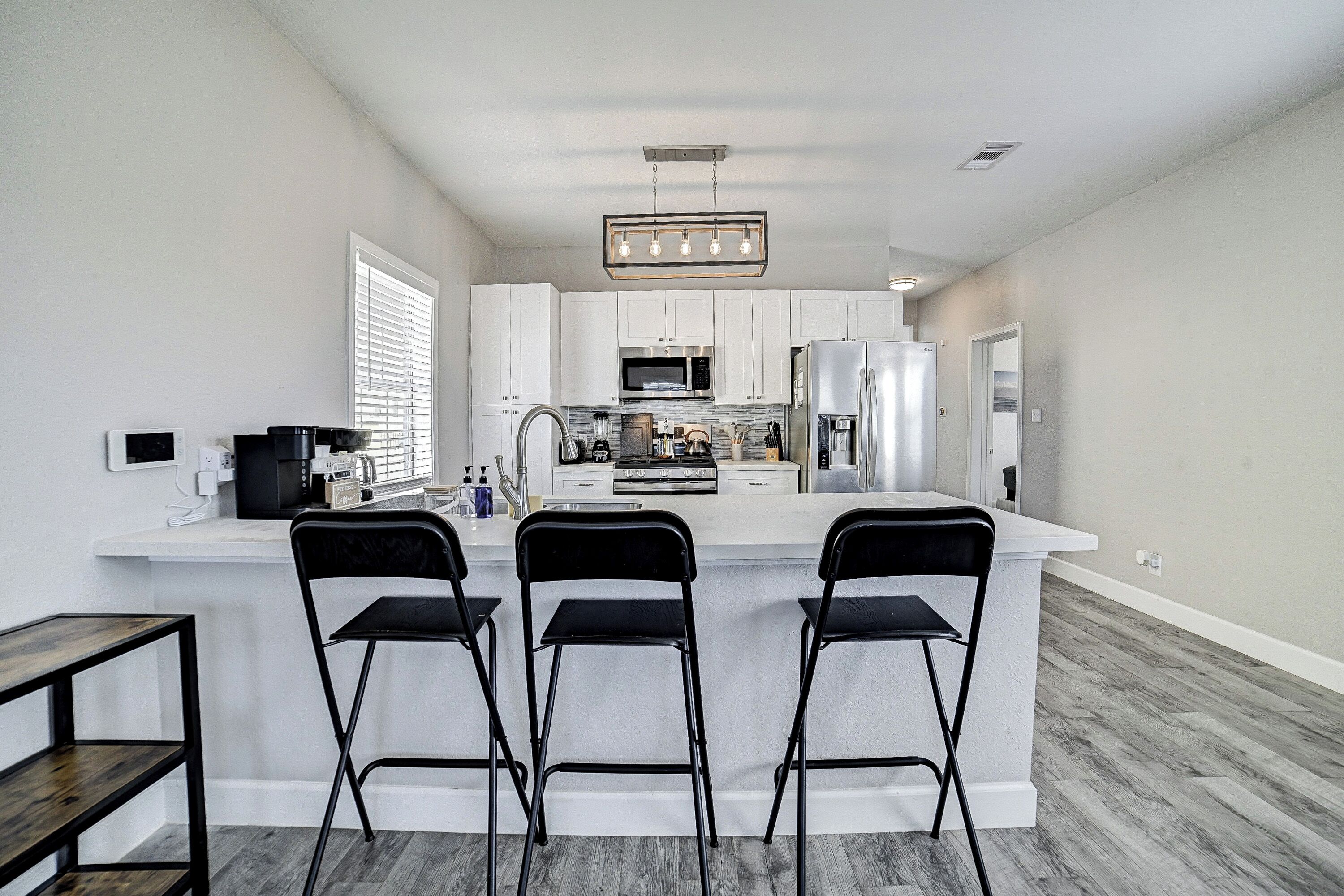 A modern kitchen with white cabinets, a central island with bar stools, stainless steel appliances, and a pendant light fixture.