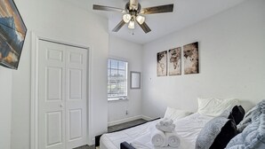Ein Schlafzimmer mit einem Bett, einem Deckenventilator, einem Fenster und Kunstwerken an der Wand.