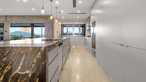 A modern kitchen with a marble island, stainless steel appliances, and pendant lighting. - Striking Luxury Home With Garden & BBQ (Margate)