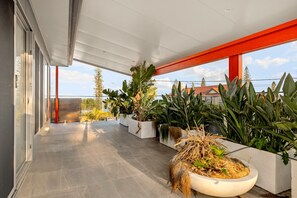 A covered outdoor area with potted plants and a view of buildings in the background. - Striking Luxury Home With Garden & BBQ (Margate)