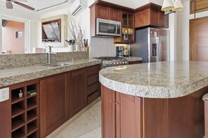 A kitchen with granite countertops, wooden cabinets, a microwave, stove, and refrigerator. - Two Bedroom Ocean View (Bajos de Chila)
