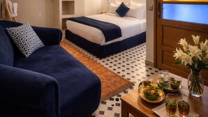 A hotel room with a bed, a sofa, a dining table with a tray of food, and a decorative vase. - Riad el fassi charme authentique  (Marrakech)