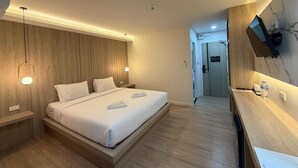 A modern hotel room with a wooden headboard, a bed with white linens, a bedside table, a TV mounted on the wall, and a wooden floor. - The Room Premium Hotel Chiangrai  (Chiang Rai)