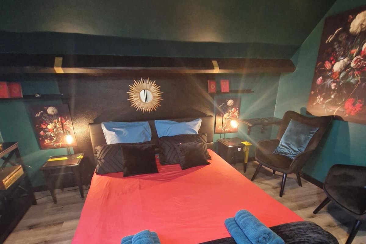 A bedroom with a bed, two nightstands, a headboard with a sun decoration, and a floral painting on the wall.