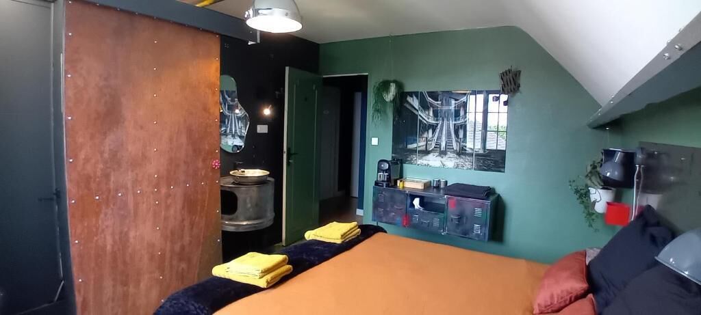 A room with a bed, a table with yellow towels, a coffee machine, and a wall-mounted TV.