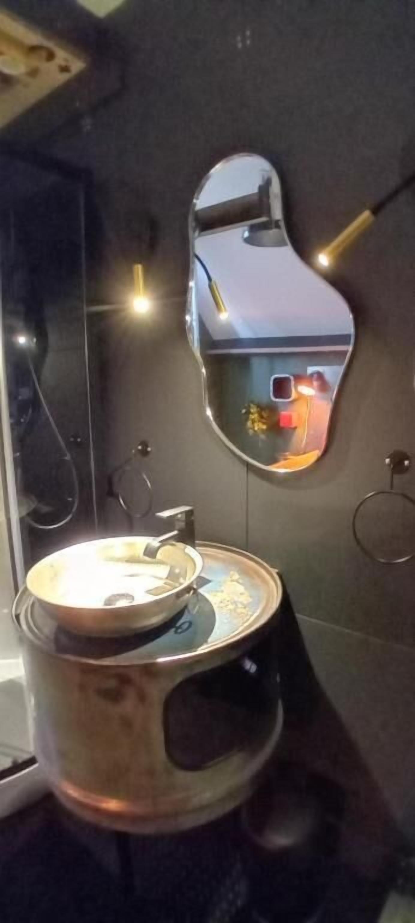 Un baño de diseño moderno, con un espejo grande, un lavabo de acero inoxidable y un inodoro.
