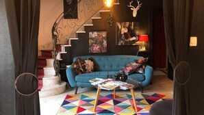 A living room with a blue sofa, a colorful geometric rug, a staircase with a metal railing, and a deer head decoration. - L'usine à rêves (Saint-Germain-du-Corbeis)