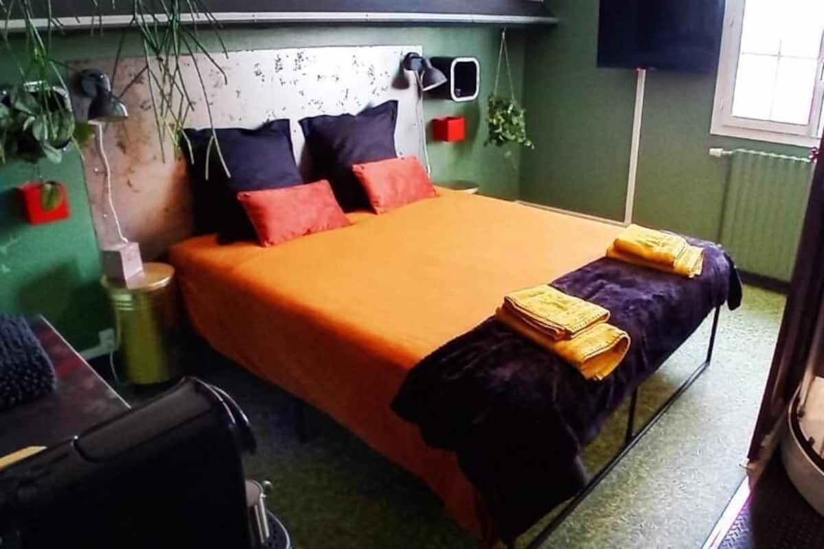 A bedroom with a bed, pillows, a nightstand, a lamp, and a window.