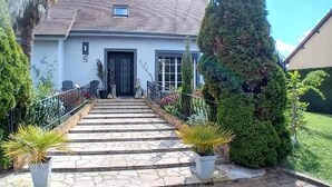 A house with a stone staircase leading to a black door, surrounded by well-maintained hedges and potted plants. - L'usine à rêves (Saint-Germain-du-Corbeis)
