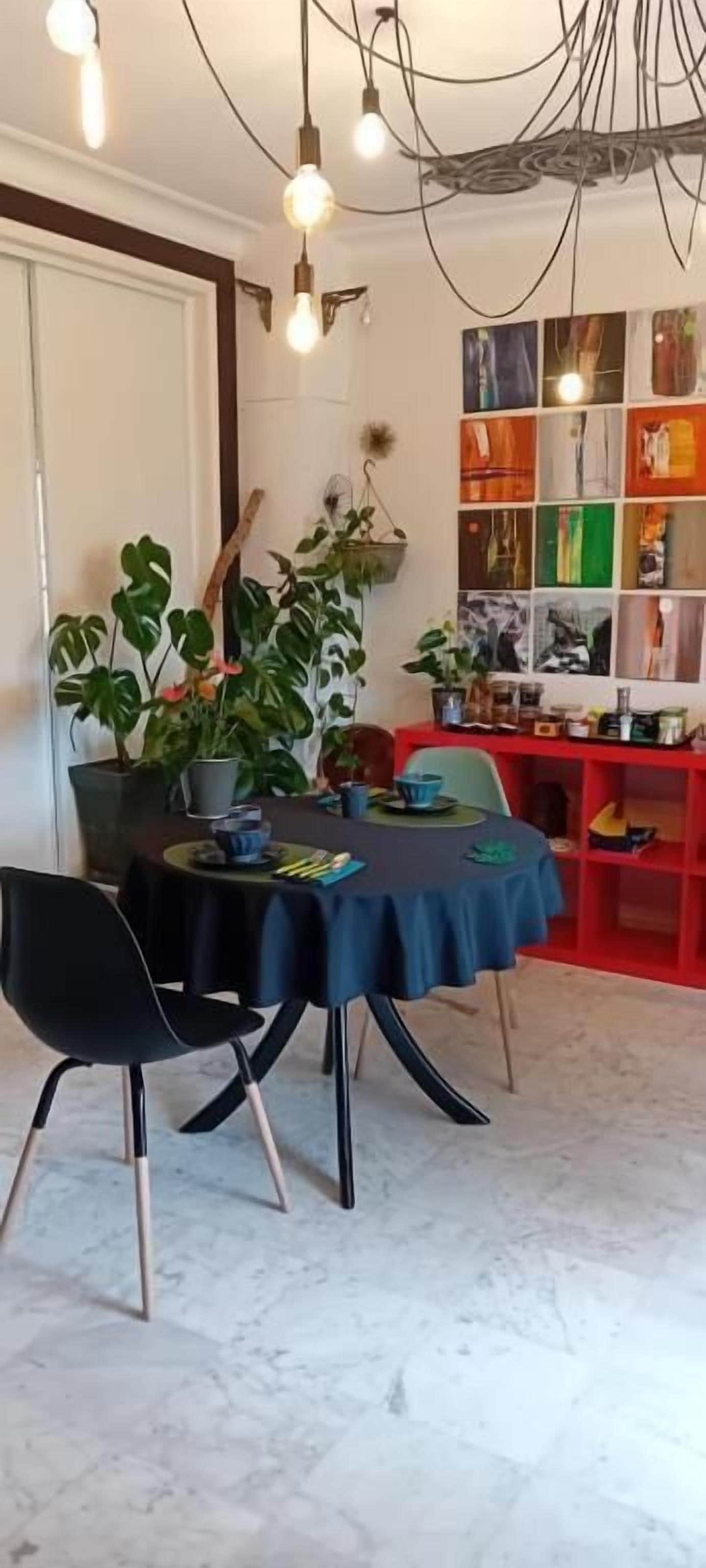 Un comedor con piso de mármol, una mesa cubierta con mantel azul, sillas negras y una planta.