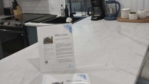 Una cocina moderna con encimera de mármol, un cartel de bienvenida y vistas al área de estar.
