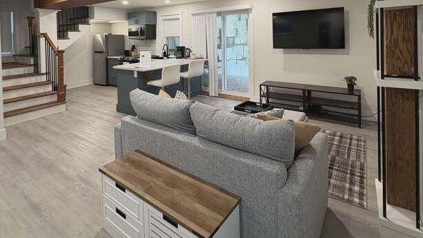 Una sala de estar moderna con un sofá gris, una mesa de centro de madera y una cocina al fondo.