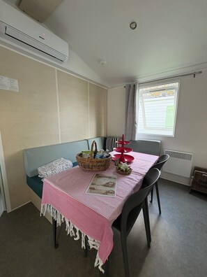 Ein Zimmer mit einem Bett, einem Tisch mit rosa Tischdecke, einem Stuhl, einem Fenster mit Vorhang und einer Klimaanlage an der Wand.