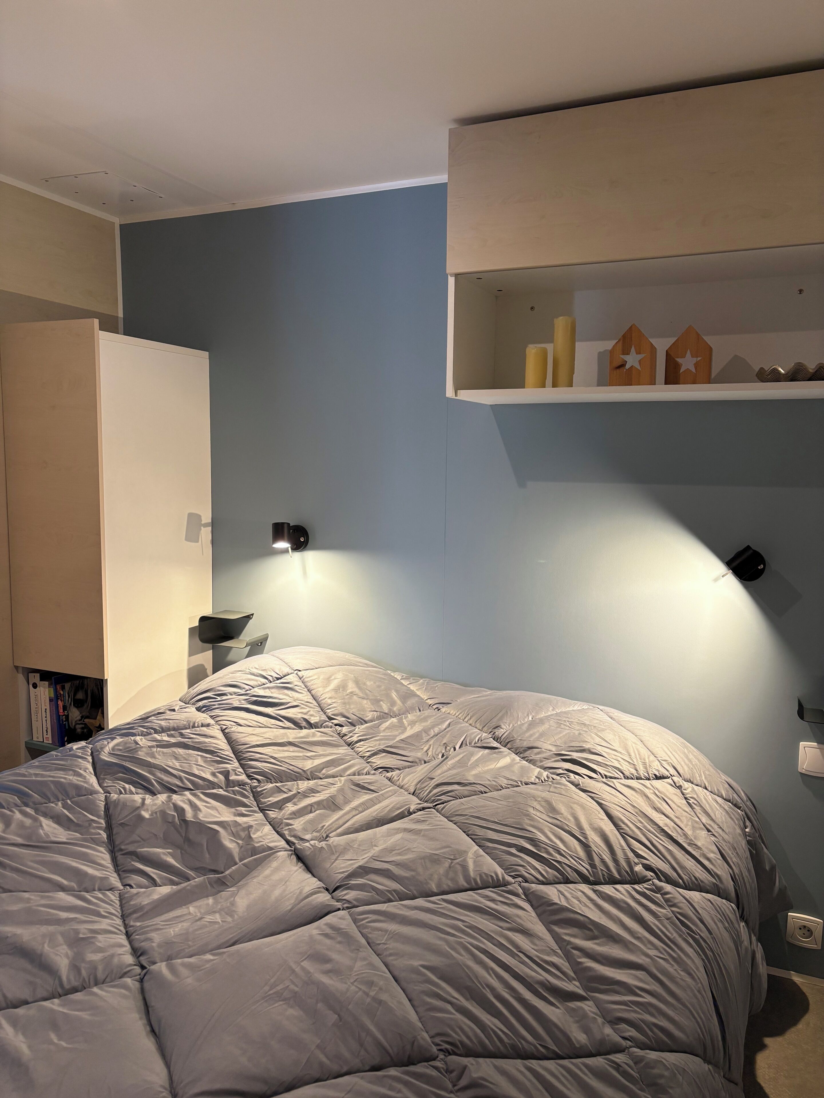 Ett sovrum med en säng, en garderob, en hylla med dekorativa föremål och en väggmonterad lampa.