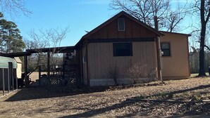 A single-story building with a gabled roof, a small attached shed, and a fenced area with a covered structure. - Cozy 2-bedroom cabin in fabulous Alba with cool AC . Only 8miles from lake fork (Alba)