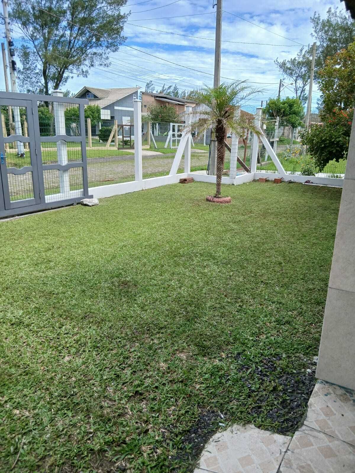 A well-maintained grassy yard with a palm tree, a white fence, and a building in the background.
