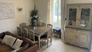A dining area with a wooden table, chairs, a vase with flowers, a cabinet with glass doors, and a wall-mounted light fixture. - VILLA PROVENCALE (Salon-de-Provence)
