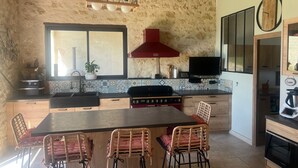 A kitchen with a large island, wooden chairs, a red range hood, and a tiled backsplash. - VILLA PROVENCALE (Salon-de-Provence)