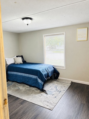 A bedroom with a bed, a window with blinds, a ceiling light, and a motivational quote on the wall. - Tranquil 2-bedroom mobile home with AC in Rocky Mount (Rocky Mount)