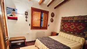 Ein Schlafzimmer mit einem Bett, einer Bank, einem Fenster mit Rollläden, einem Heizkörper und einem Wandteppich.