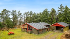 A cabin with a red roof and wooden walls, a picnic table, and a swing set in a grassy yard surrounded by trees. - "Samine" - 1.2km from the sea by Interhome (Blåvand)