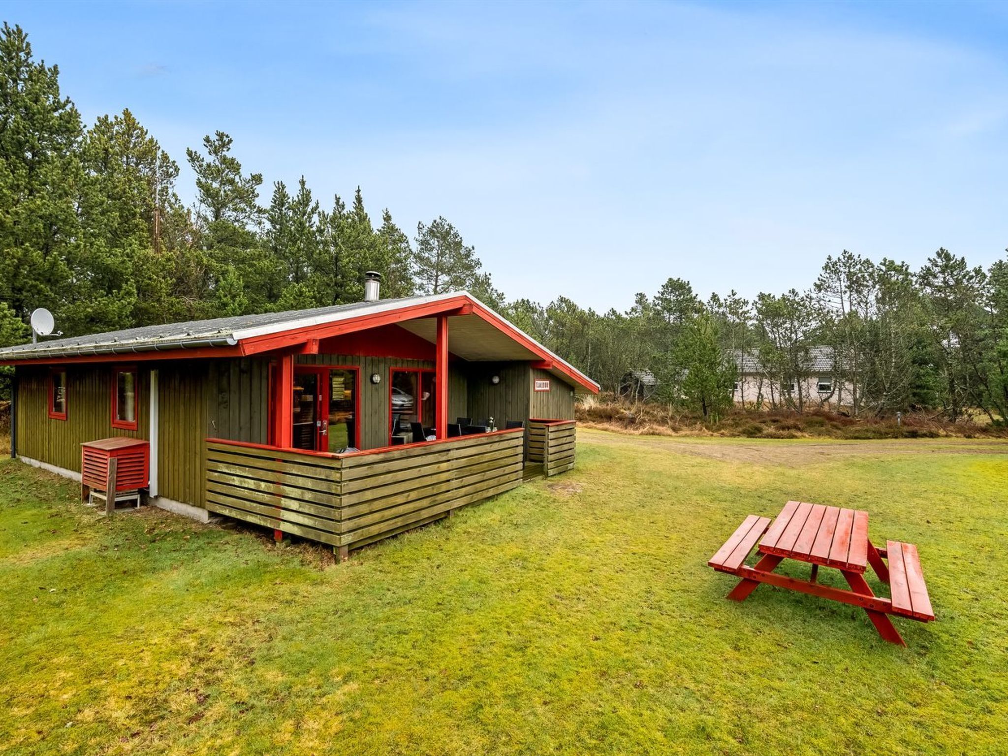 Een rustieke blokhut met een rood dak en houten wanden, een picknicktafel en een schotelantenne.