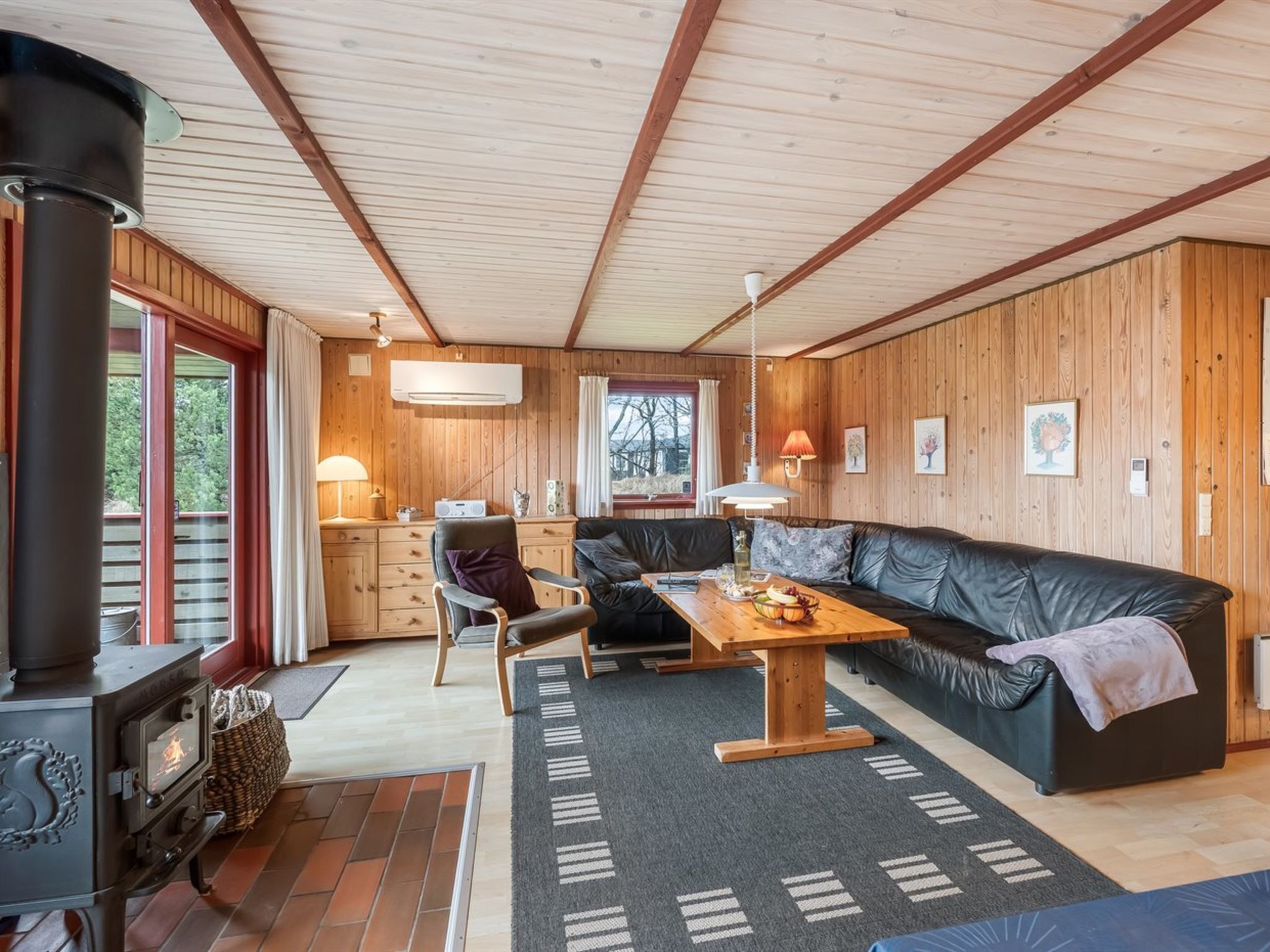 A cozy cabin interior with a wooden interior, a sofa, a dining table, a fireplace, and a kitchen area.