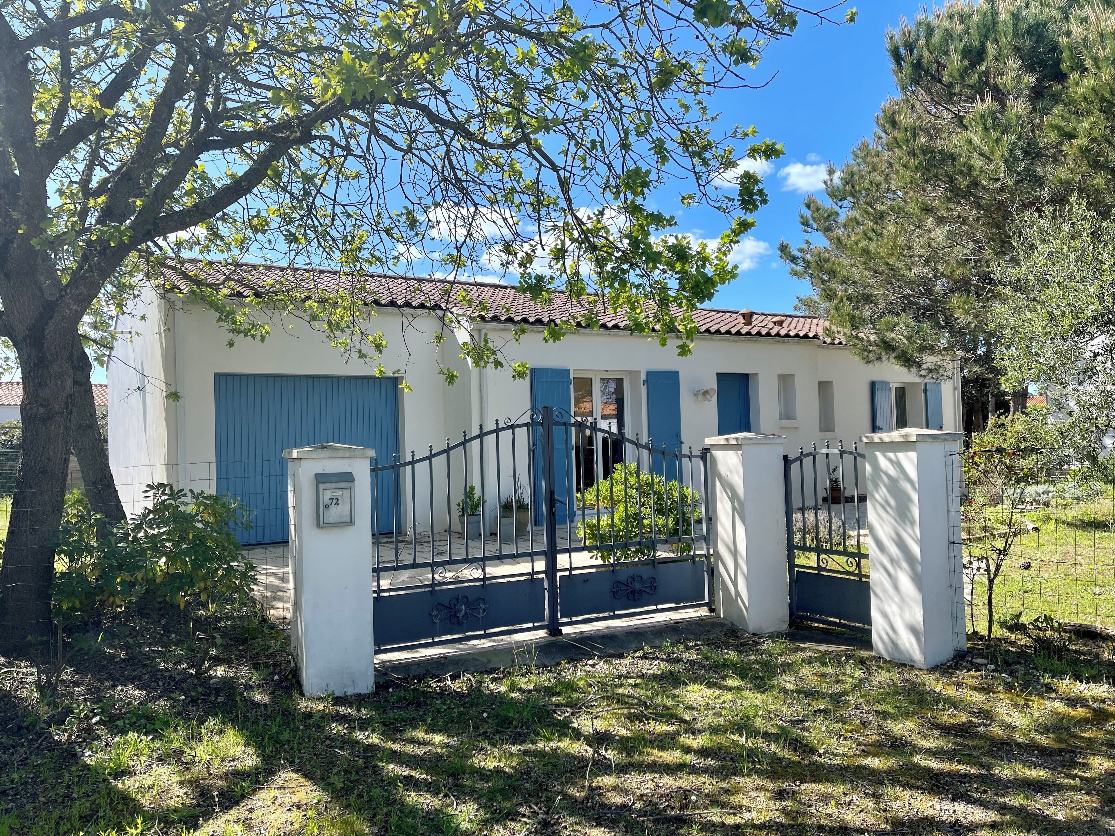 A white building with blue shutters, a metal gate, and a tree in the foreground.