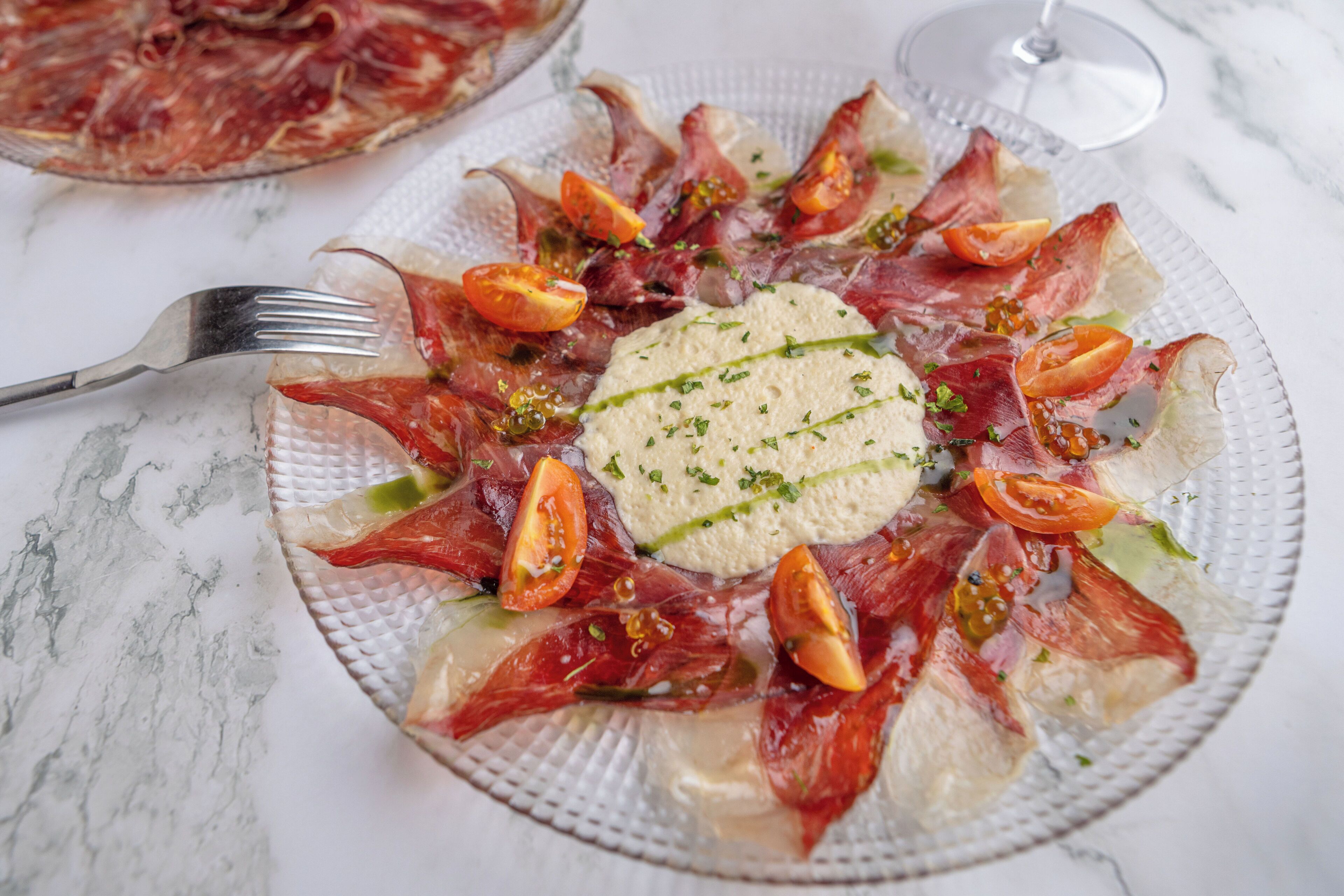 A plate of food with prosciutto, tomatoes, and a green garnish.