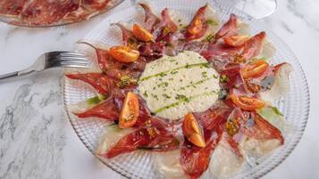 A plate of food with prosciutto, tomatoes, and a green garnish.