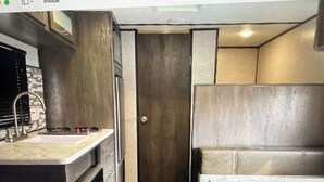 Eine kleine Küchenzeile mit Spüle, Herd und Backofen. Ein kleiner Essbereich mit Tisch und Bank vorhanden.