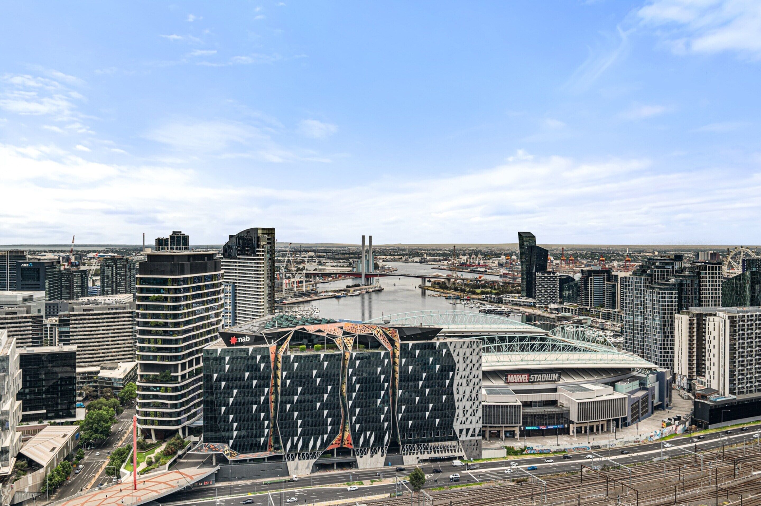 Un paysage urbain moderne, avec un bâtiment remarquable à la façade géométrique originale, et un stade en premier plan.