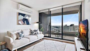 A modern living room with a sofa, a TV, and a view of a cityscape through large sliding doors.