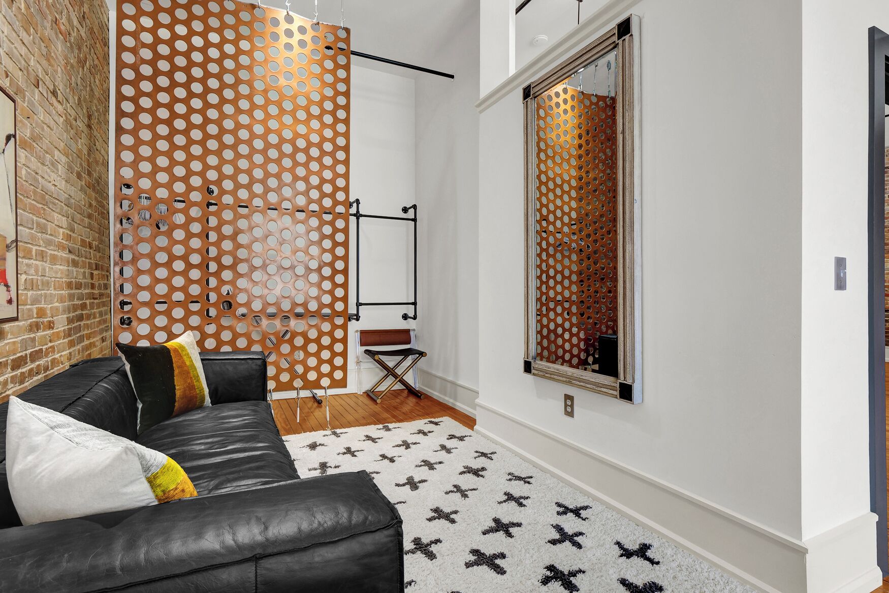 Una sala de estar moderna con un sofá de cuero negro, alfombra estampada y un espejo grande.