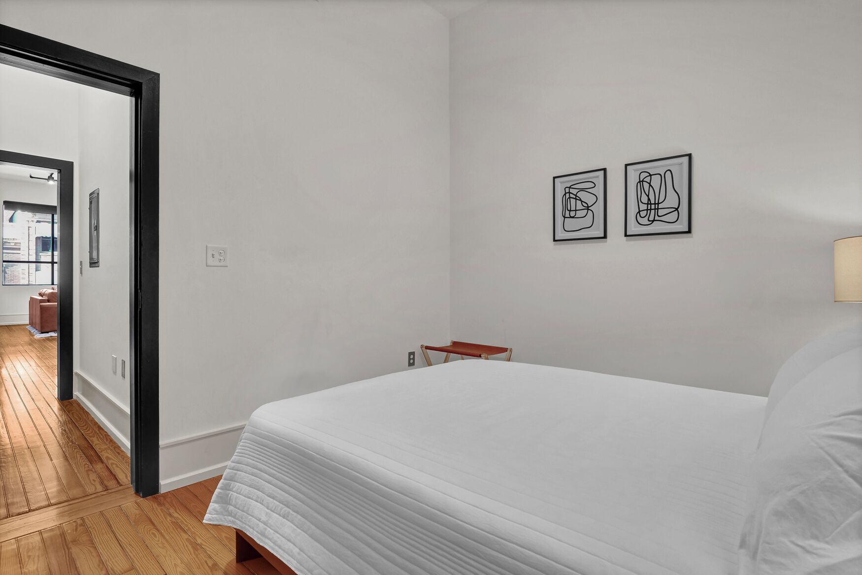 Un dormitorio con una cama, una mesita de noche y dos obras de arte abstractas en la pared.