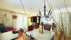 Una sala de estar con sofá, una mesa de comedor con sillas, una araña y una cocina al fondo.